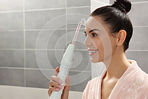 Woman using high frequency darsonval device in bathroom, space for text