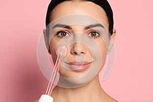 Woman using high frequency darsonval device on pink background photo