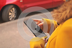 Woman using and holding modern mobile phone in hand on the street near to cafe with parking. Connection and