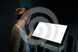 Woman using interactive empty white touchscreen display kiosk at exhibition