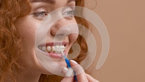 Woman Using Interdental Brush Cleaning Teeth With Brackets, Beige Background