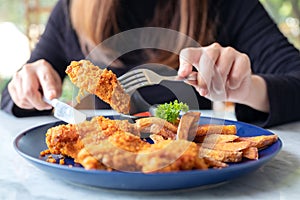 A woman using knife and fork to eat fried chicken and french fries in restaurant