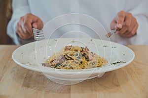 A woman using knife and fork to eat spicy bacon spaghetti on wooden table