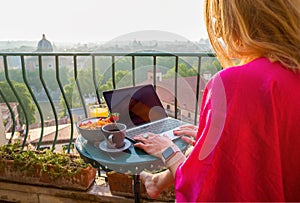 Woman using laptop during breakfast on balcony