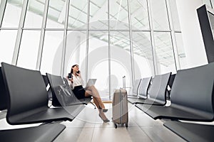 Woman using laptop computer at airport terminal sitting with luggage suitcase for business travel waiting flight