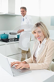 Woman using laptop and man cooking food