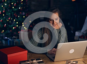 Woman using laptop, shopping online, using credit card at home. Christmas tree in the background