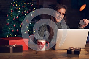 Woman using laptop, shopping online, using credit card at home. Christmas tree in the background