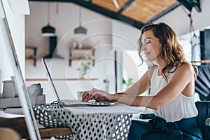 Woman using laptop while sitting at home. Young woman sitting in kitchen and working on laptop.