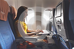 Woman using laptop while is sitting in plane near window.