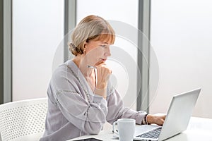 Woman using laptop and smartphone at home, Mature woman checking their bills