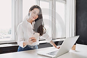 Woman using laptop and smartphone in office. Beautiful girl working at home.