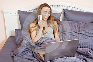 Woman using laptop for store online shopping in bed at home, payment by credit card with online transaction banking. Happy Girl