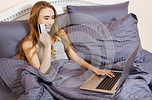 Woman using laptop for store online shopping in bed at home, payment by credit card with online transaction banking. Happy Girl