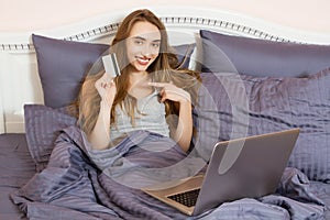 Woman using laptop for store online shopping in bed at home, payment by credit card with online transaction banking. Smile Girl