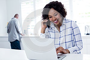 Woman using laptop while talking on mobile phone
