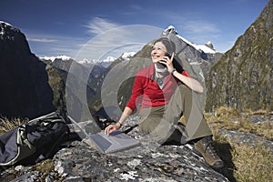 Woman Using Laptop And Walkie Talkie Against Mountains