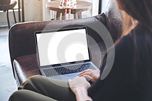 A woman using and looking at laptop with blank white desktop screen while sitting on sofa