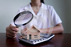 Woman using a magnifying glass to house model and calculator. Searching housing and home insurance concept