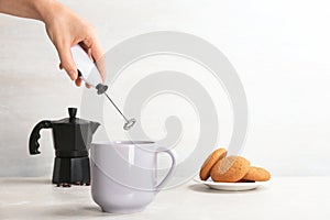 Woman using milk frother in cup on table