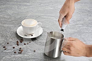Woman using milk frother in pitcher near cup