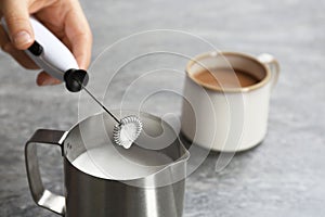 Woman using milk frother in pitcher near cup photo