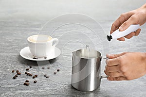 Woman using milk frother in pitcher near cup of coffee