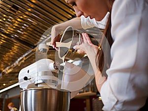 Woman using mixer standing at counter in her apron. Making dessert in pastry shop