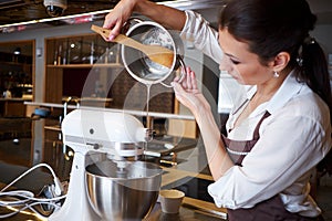 Woman using mixer standing at counter in her apron. Making dessert in pastry shop