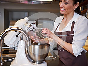 Woman using mixer standing at counter in her apron. Making dessert in pastry shop
