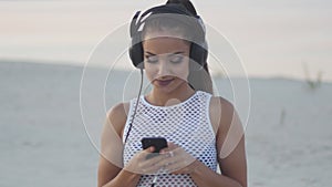 Woman using mobile cell smart phone on beach wearing earphones for music or talking Girl in bikini using smartphone