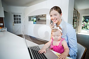 Woman using mobile phone with baby girl by laptop