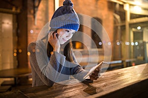 Woman using mobile phone at bar counter in coffee shop at night