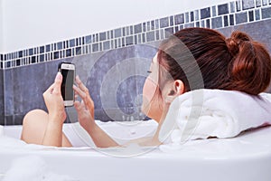 Woman using mobile phone in bathtub in bathroom