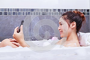 Woman using mobile phone in bathtub in bathroom