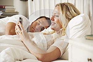 Woman Using Mobile Phone In Bed Whilst Husband Sleeps