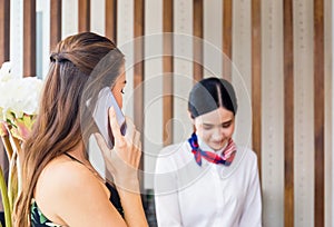 Woman using mobile phone with blurred female receptionist standing at hotel counter