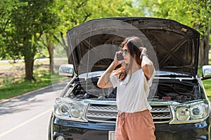 Woman using mobile phone calling for assistance with broken down car engine on street