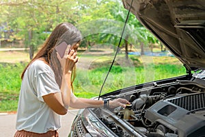 Woman using mobile phone calling for assistance with broken down car engine on street