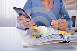 Woman Using Mobile Phone With Diary