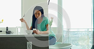 Woman using mobile phone while having breakfast in kitchen 4k