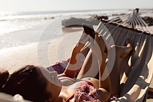 Woman using mobile phone while relaxing in a hammock on the beach