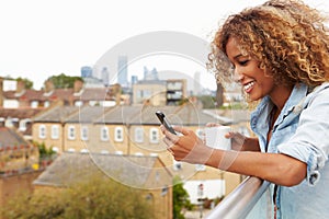 Woman Using Mobile Phone On Rooftop Garden Drinking Coffee