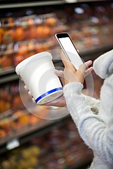 Woman using mobile phone while shopping for grocery