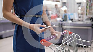 Woman using mobile phone while shopping in supermarket, trolley mall grocery shop store
