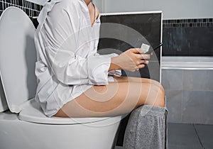 Woman using mobile phone and sitting on toilet