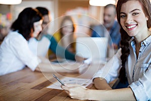 Woman using mobile phone while team working in background