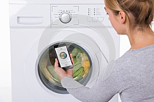 Woman Using Mobile Phone To Operate Washing Machine