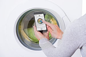 Woman Using Mobile Phone To Operate Washing Machine