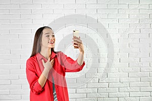 Woman using mobile phone for video chat against brick wall